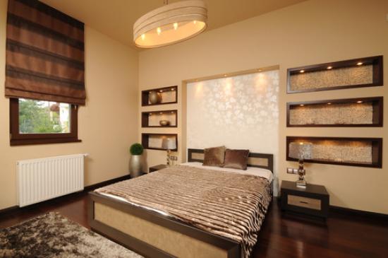 Vackra gipsskivor med dekorativ belysning på väggen vid sängens huvud i sovrummet