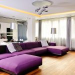 Didelė violetinė sofa sujungta svetainė-virtuvė