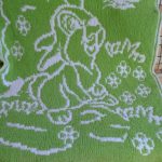 Green and white blanket with a bunny on a meadow