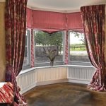 Long maroon curtains na may isang pattern para sa isang bay window sa kuwarto