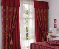 Double burgundy curtains with lambrequin grabs and tulle in the bedroom