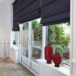 Czarne rzymskie zasłony na oknach i drzwiach salonu z wyjściem na taras