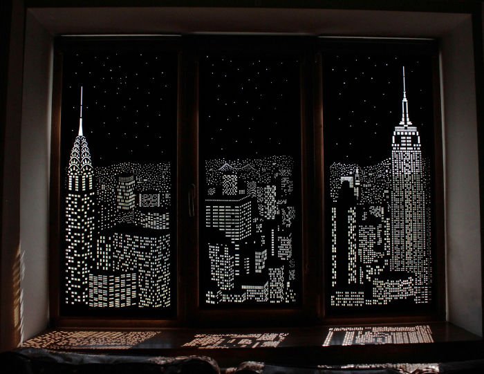 Rolowane zasłony z perforowanym miastem nocą na oknie PCV