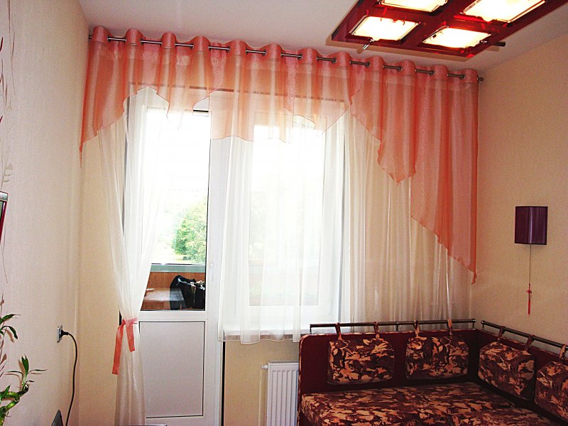 Röd lambrequin av transparent tulle på balkongfönstret