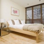 Дървено легло в спалнята с щори на прозорците